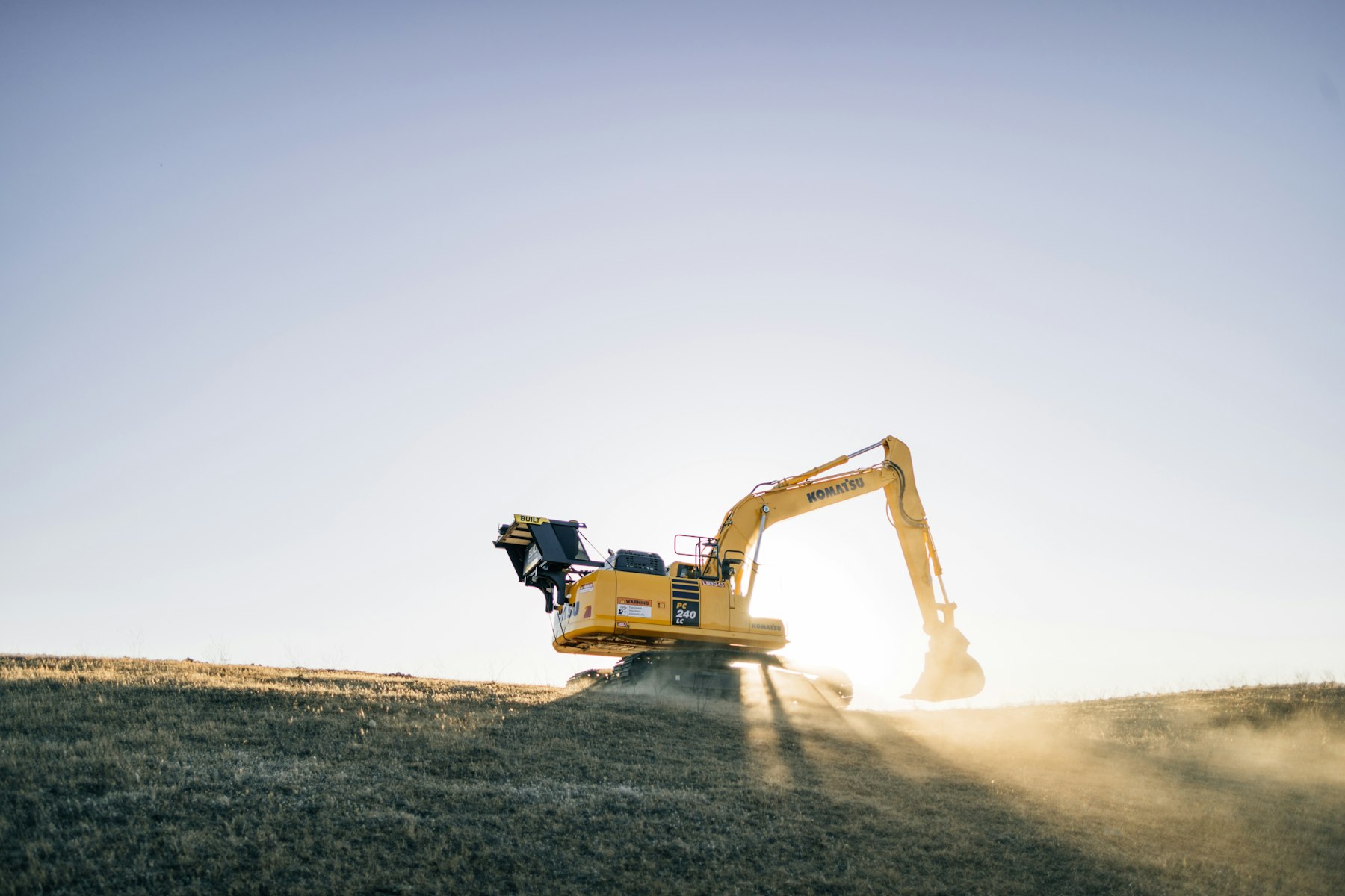 A yellow excavator on a hill under a blue sky