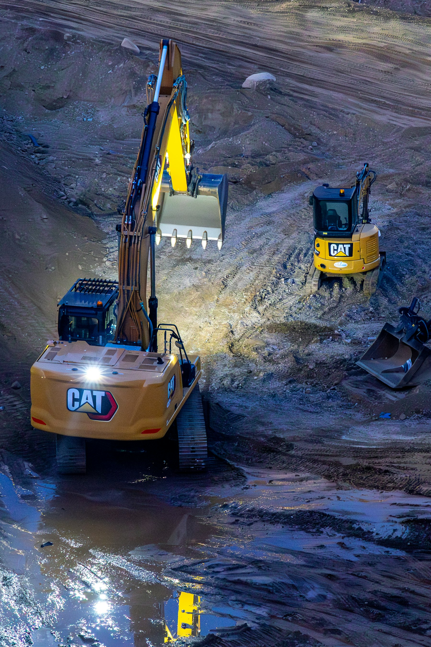 Two excavators working on a construction site at night